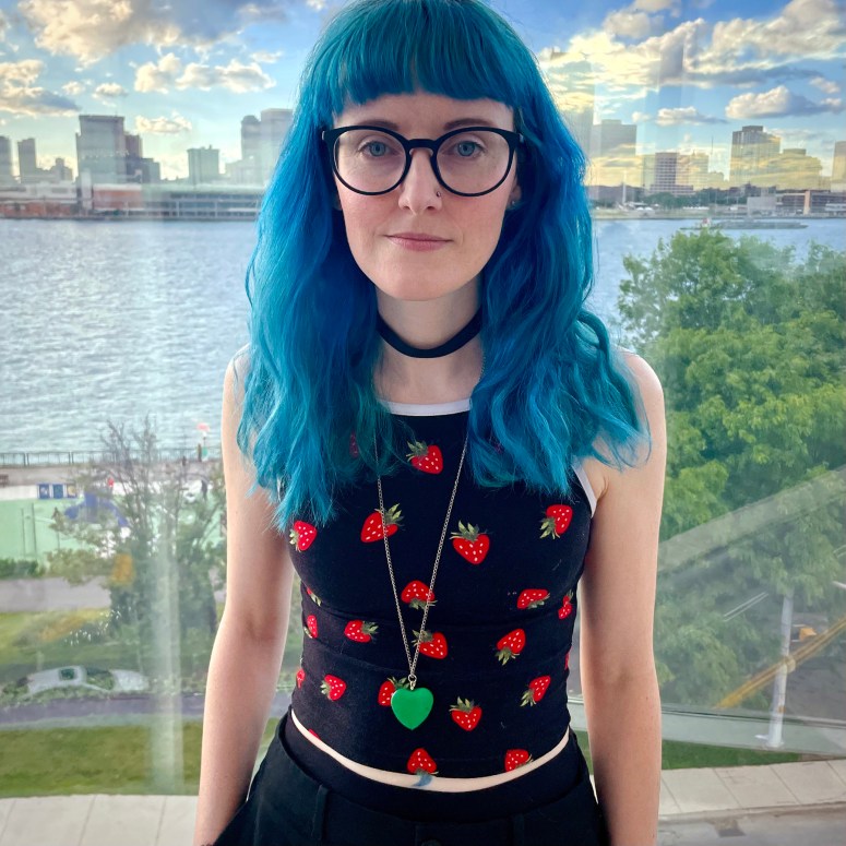 Jade Wallace stands in front of a window that shows the Detroit River and a cluster of trees behind them.
